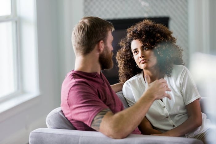 A man and woman sitting on a couch and having a serious conversation.