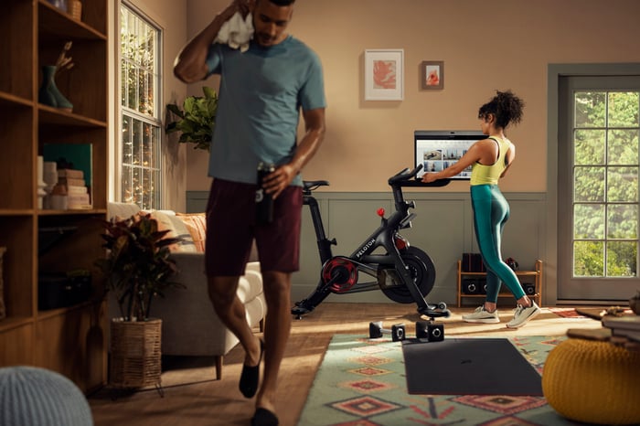 A person adjusts the screen on a Peloton bike in a living room.