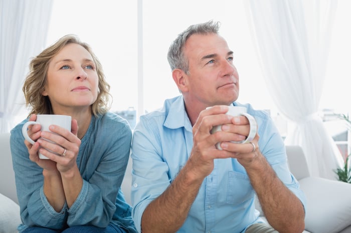 A married couple sitting together while looking thoughtful.