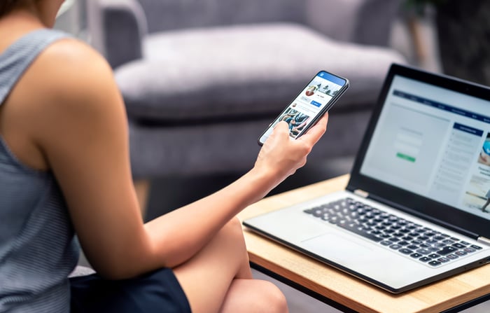 A person on their phone in front of a computer.