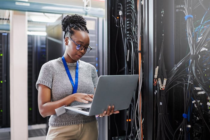 A person working in a server room on a laptop.