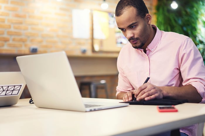 An investor studies something on a laptop and takes notes.