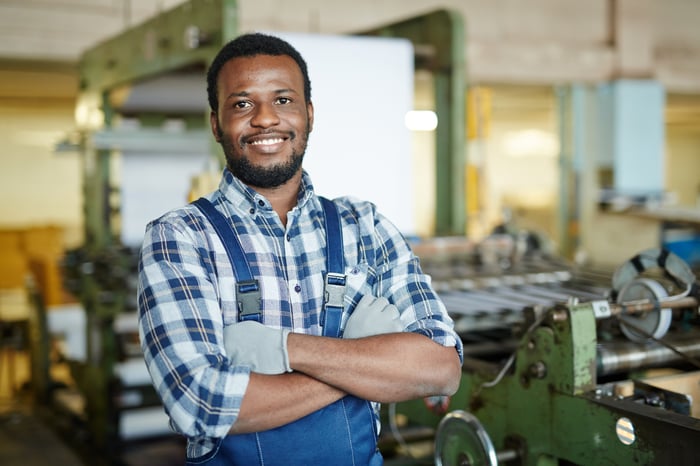 Someone is in a factory, smiling with arms crossed.