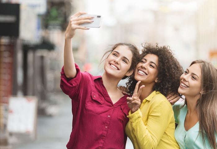 Three friends taking a smiling selfie with a smartphone.