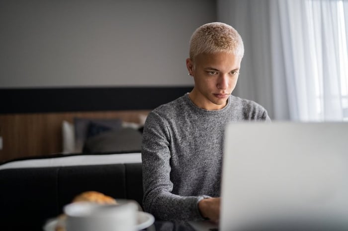 A young adult uses their laptop at home during breakfast.