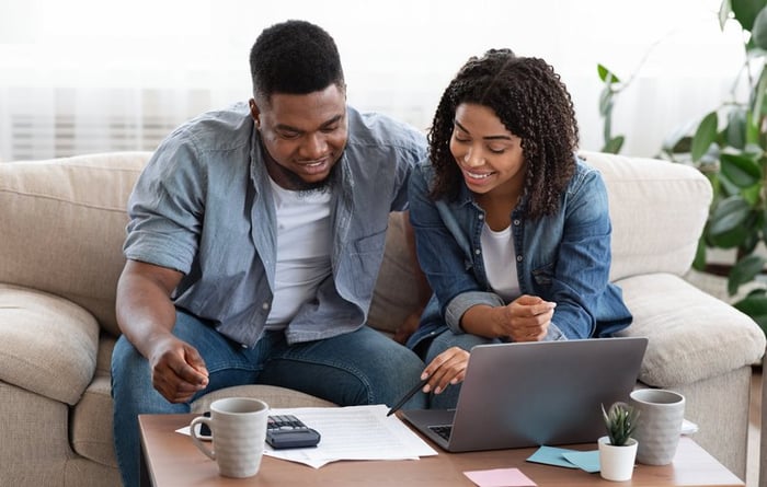 Couple using laptop and calculator together smiling.