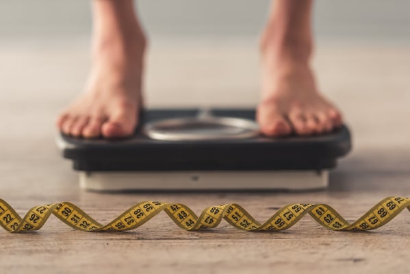 A person standing on a scale with a tape measure on the ground.