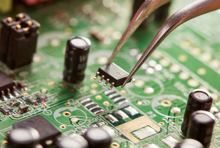 A tweezer holding a computer chip over a circuit board.