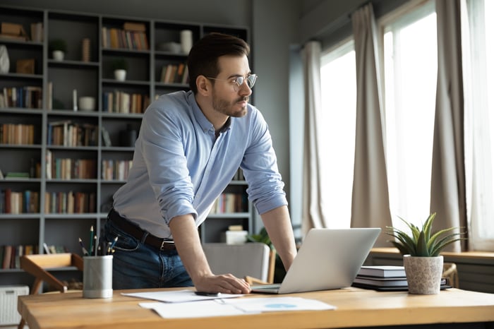 An investor, standing near a desk, looks pensively out the window.