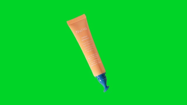 Close up of a pink bottle holding eye cream on a green background