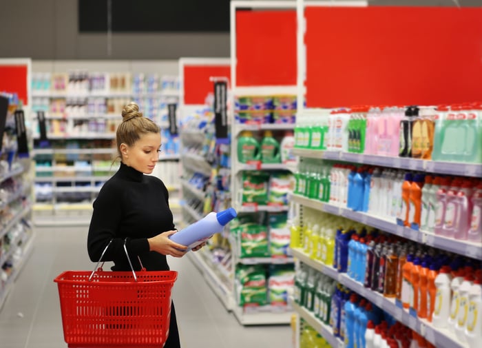 Person examining a cleaning product in a grocery store aisle.