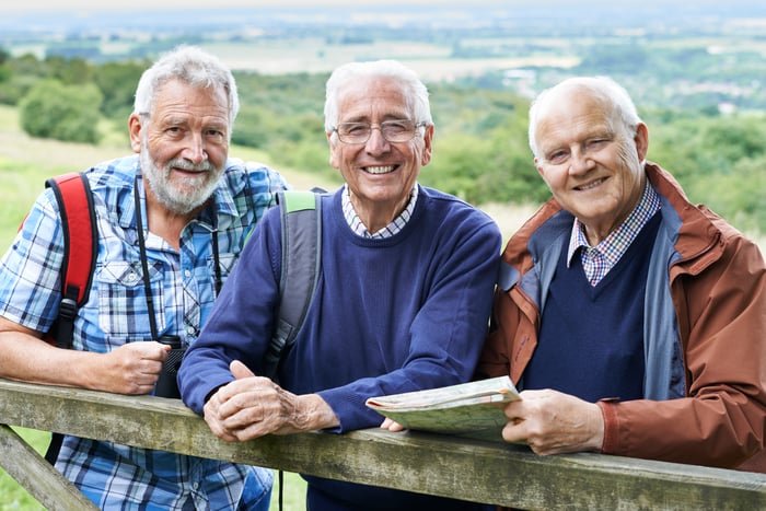 Three people outside leaning on a wooden fence.