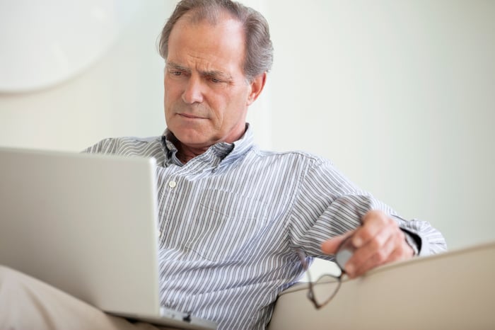 A person sitting on a couch who's critically reading material on their laptop.