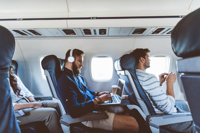 Three people sitting in consecutive aisle seats on an airplane.