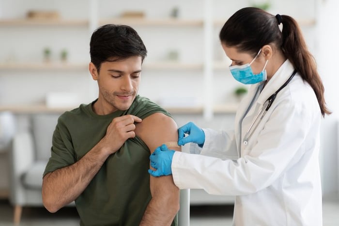 Healthcare worker putting bandaid over vaccine injection site on person's upper arm.