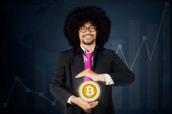 A person in a suit holds a glowing Bitcoin sphere in front of a rising chart.