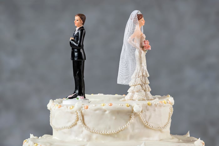 Bride and groom figurines atop wedding cake, facing away from each other.