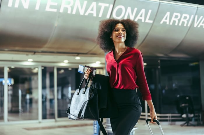 Smiling traveler walks through airport with luggage in tow.