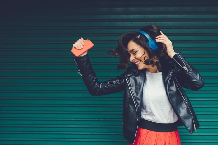 A person smiling and dancing with headphones on while holding a smartphone.