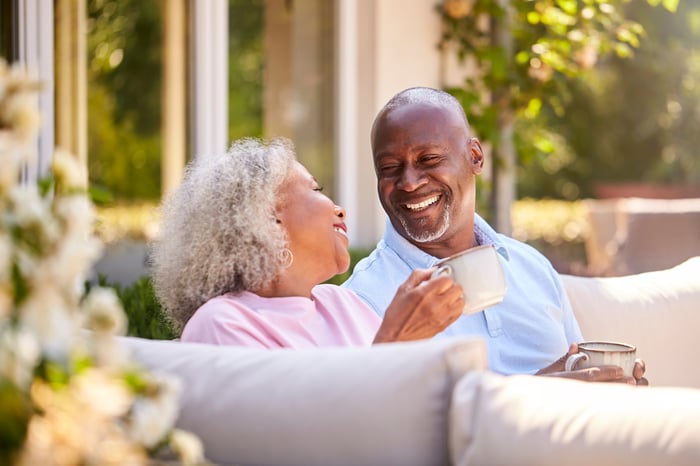 A senior couple smiling at each other drinking coffee outdoors.