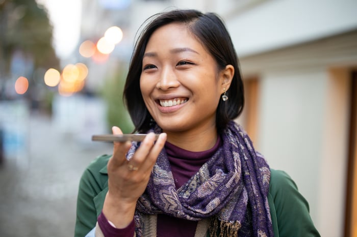 A person using the speaker function on their smartphone while walking on a city street. 