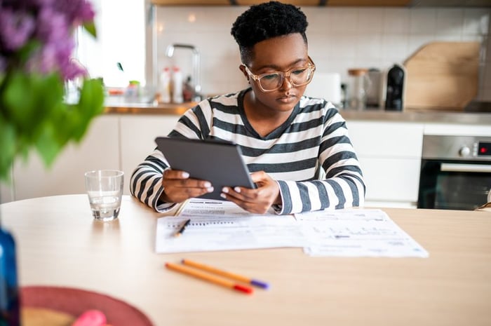 A person looks over paperwork and uses a tablet in their kitchen.