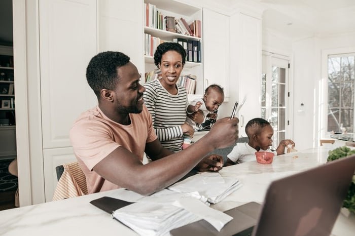 A couple reviews their financial documents in their kitchen while watching their children.