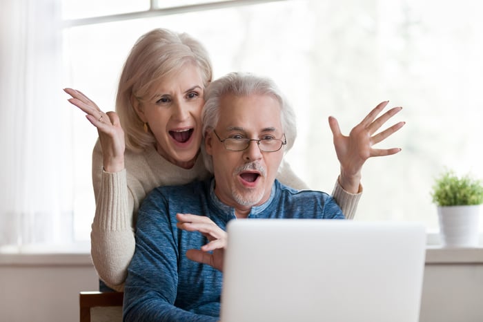 A couple is looking at an open laptop and looking amazed and happy.