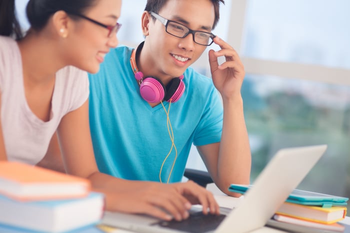 Two college students reading material on a shared laptop.