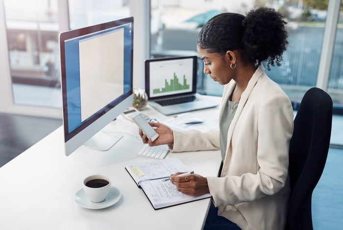 An investor checks a portfolio on multiple screens at an office desk.