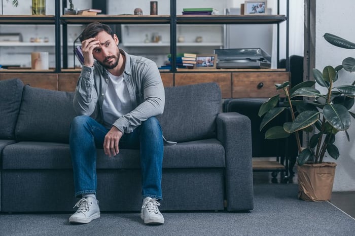 An upset man sitting on a couch with his hand on his head.