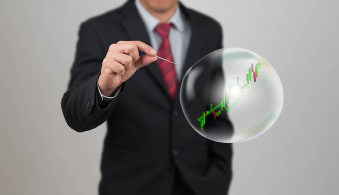 A person in a suit about to pop a bubble with a stock chart on it.