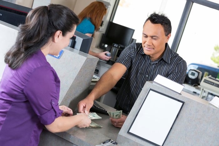 A young woman is at the bank. A teller is counting out her money.