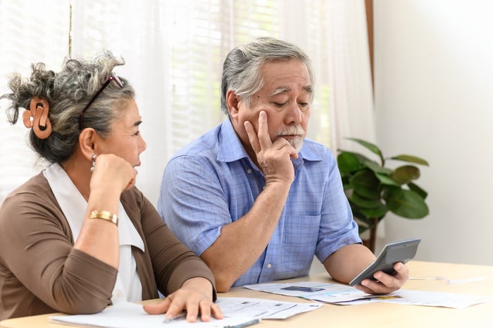 A visibly worried couple analyzing their bills and financial statements while seated at a table in their home.