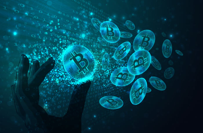 An artist's rendering of a silhouette of a hand reaching for glowing circles that look like coins and contain the Bitcoin logo.