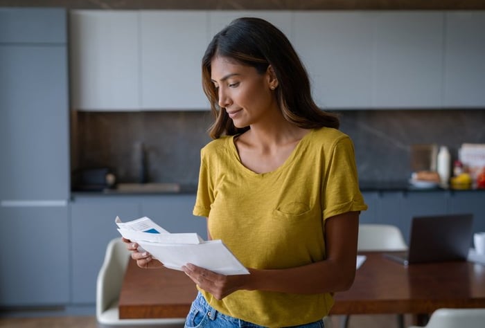 A smiling person opening their mail while standing in the kitchen.