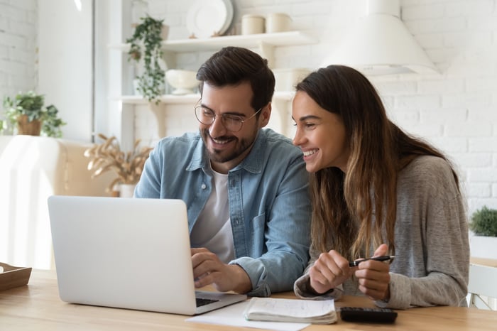 Two people sit in a living room and look at something on a laptop.