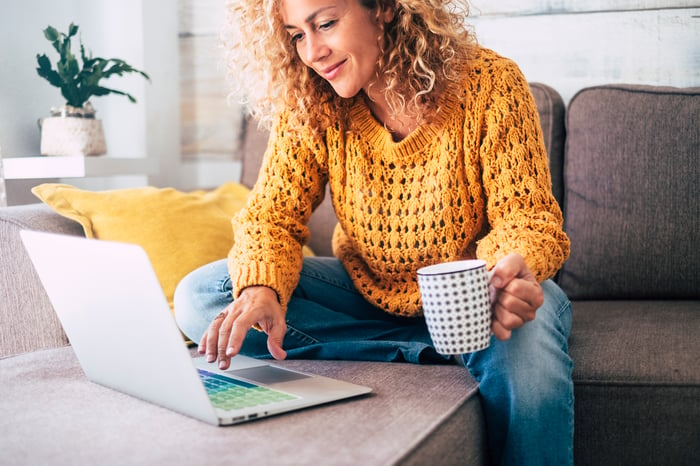 A person on a couch using a laptop and holding a mug.