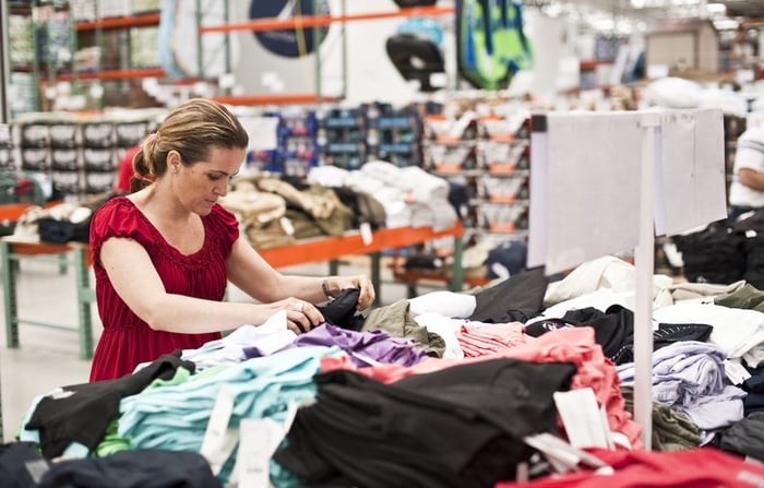 Shopper looking through piles of clothing at warehouse club store.