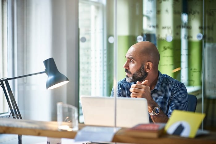 Mature man at desk looking off in thought.