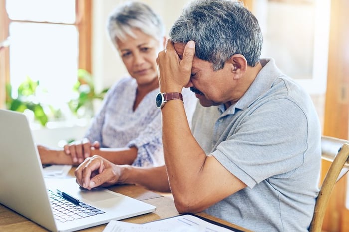 Mature couple appears distraught while looking at laptop.