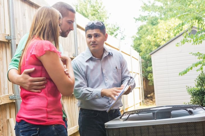 An air conditioner repairman uses a clipboard to explain the cost of repairs to the homeowners.