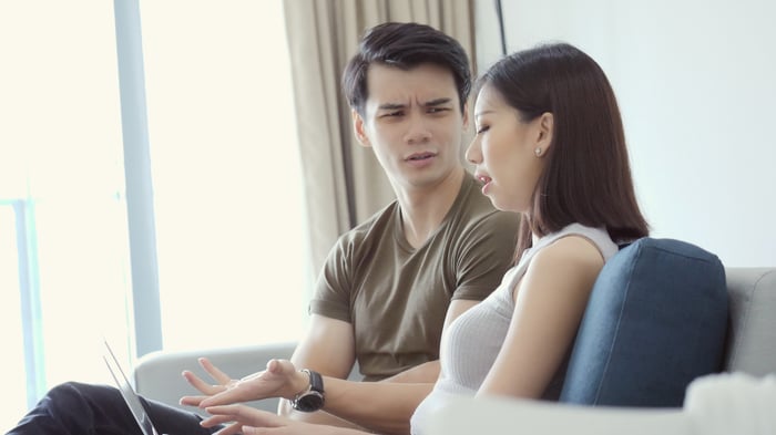 Two people discussing something while one of them looks at a laptop.