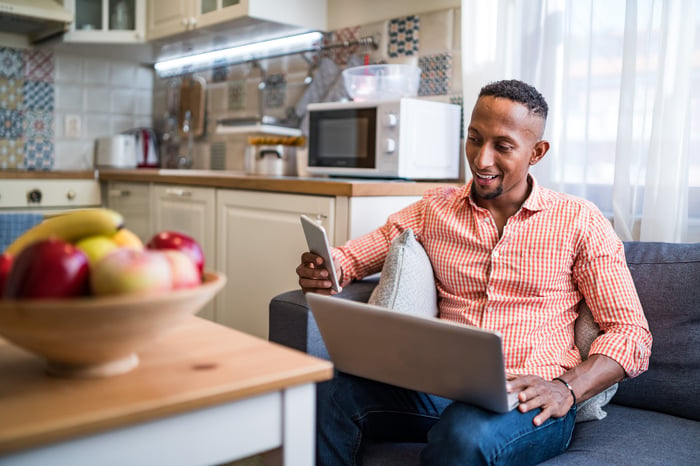 A person with an open laptop on their lap who's engaged with a smartphone in their right hand.