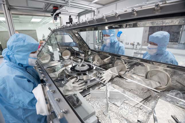 The OSIRIS-REx team pouring the final portion of asteroid rocks and dust into sample trays below.