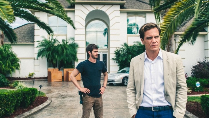 Andrew Garfield stands behind Michael Shannon in front of a house in 99 Homes.