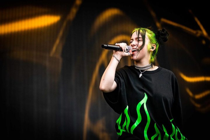 Billie Eilish holds a mic and sings.