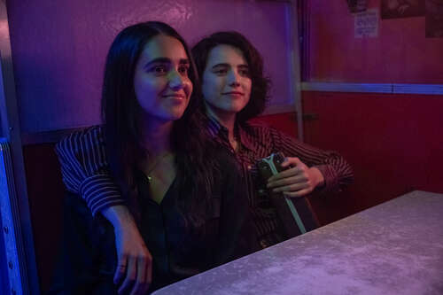 Geraldine Viswanathan and Margaret Qualley hold a briefcase and each other in a still from Drive-Away Dolls