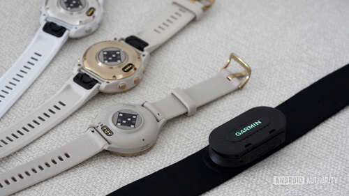 A variety of Garmin devices rest face down displaying their heart sensors, alongside the Garmin HRM Fit.