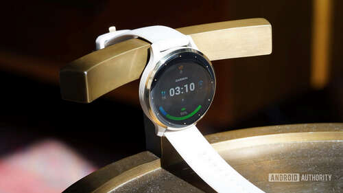 A Venu 3 rests on a gold stand, displaying a watch face.